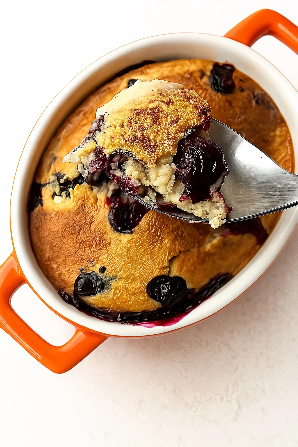 A spoonful of blueberry cottage cheese breakfast bake being lifted from an orange baking dish.
