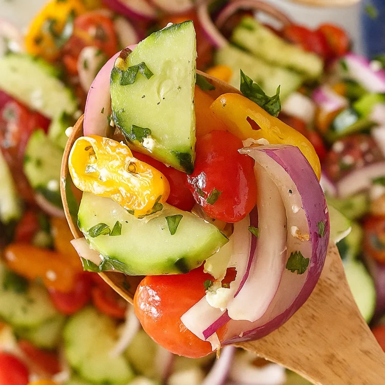 A spoon scooping fresh cucumber tomato salad with herbs